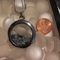 Silver pendant with stones on a bed of white marbles next to a penny