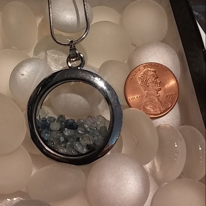 Silver pendant with stones on a bed of white marbles next to a penny
