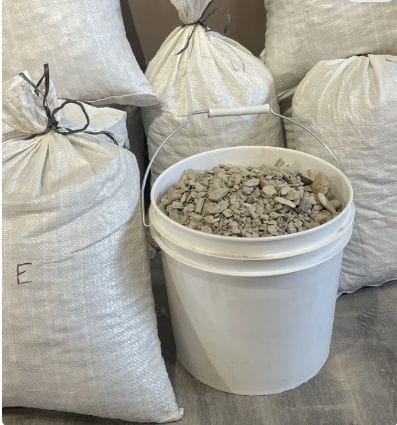 Bucket filled with gem mining material next to large gravel bags